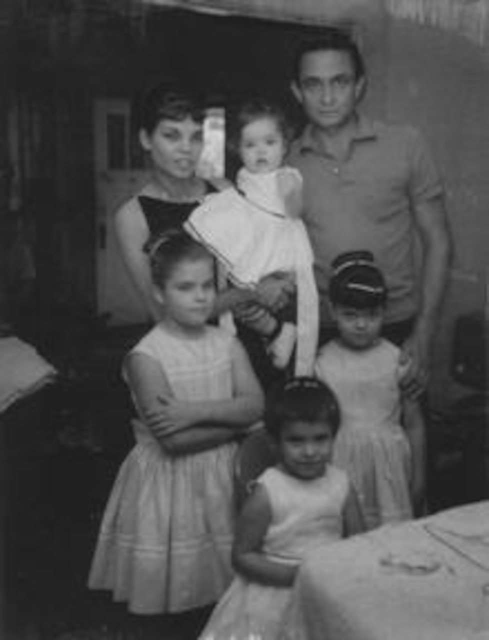 Four girls in white dresses and a man and a woman in civilian attire pose for a photo. The woman is holding one of the young girls.