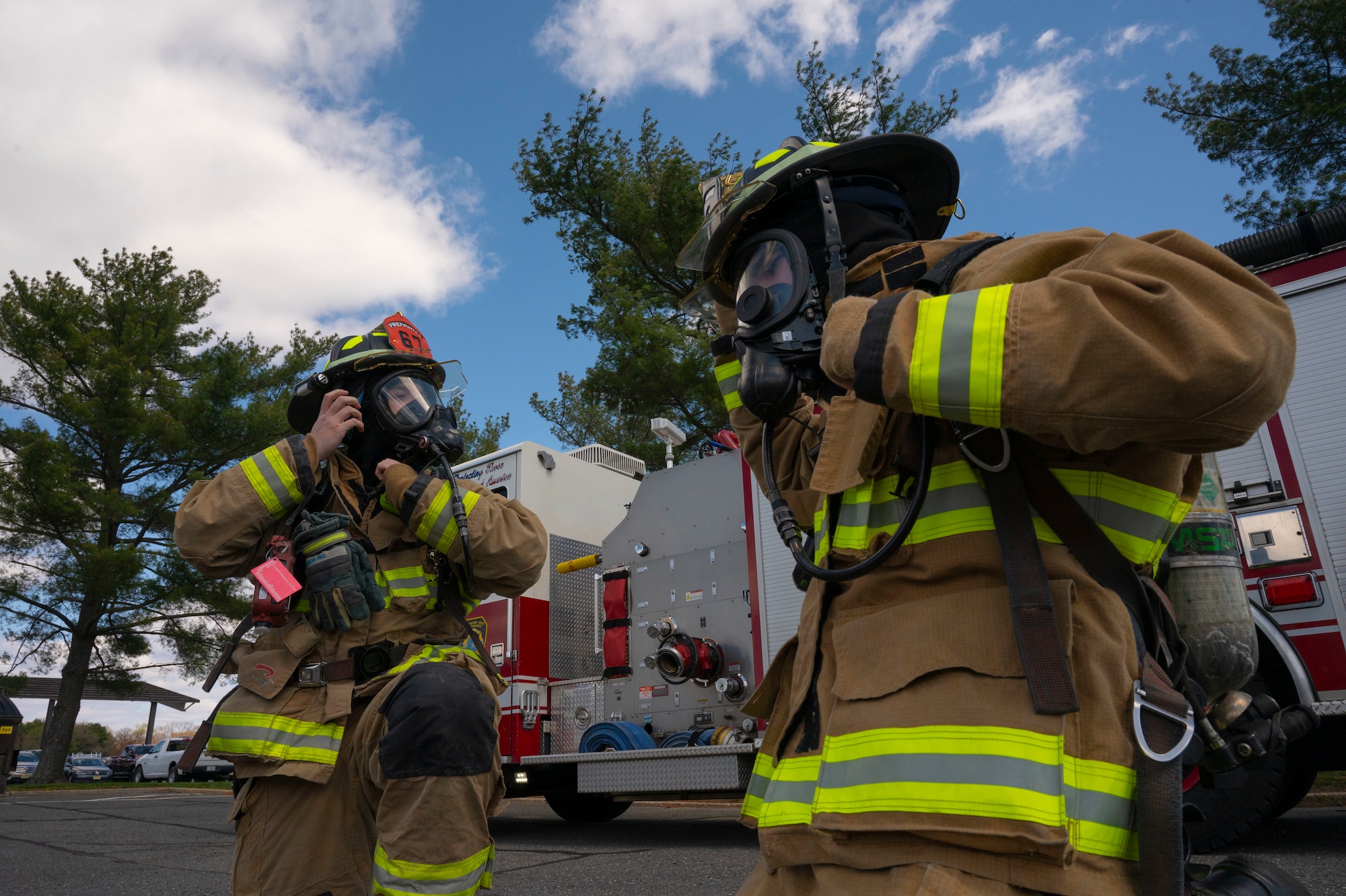 U.S. Air Force Staff Sgt. William Shupe and Senior Airman Joshua Talijan, 87th Civil Engineer Squadron firefighters, don their self-contained breathing apparatus (SCBA) as they prepare to respond to a simulated fire during Operation Honey Badger (OHB) at Joint Base McGuire-Dix-Lakehurst, N.J., April 8, 2025. OHB is an exercise organized by the 87th Civil Engineer Squadron to prepare Airmen for real-world situations and promote mission readiness. (U.S. Air Force photo by Airman 1st Class Luisa E. Dugan)