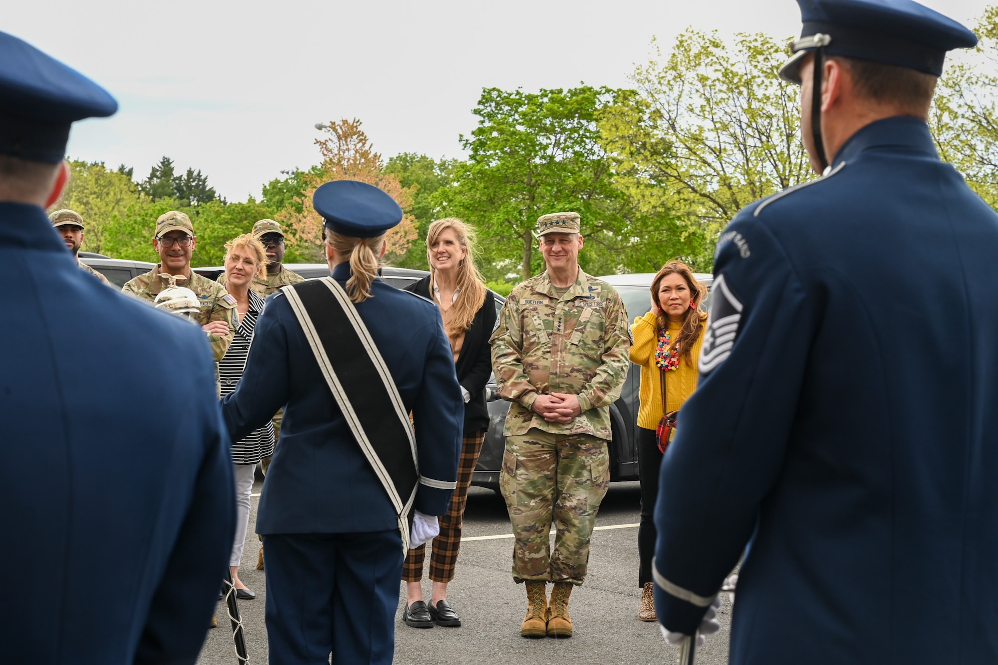 Photo of an Air Force Band members standing while in a band formation while U.S. Space Force leaders watch the performance in the background.