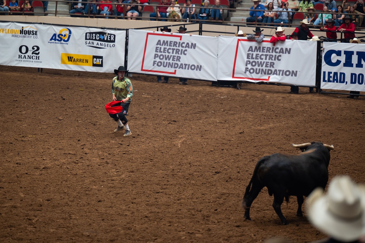 A rodeo clown distracts a bull during the bullfighting event at the San Angelo Stock Show & Rodeo at the Foster Communications Coliseum, San Angelo, Texas, April 16, 2025. Bullfighting is a timed rodeo event where a fighter avoids the bull by dodging, jumping, and using barrels to hide. (U.S. Air Force Photo by Airman 1st Class Brian Lummus)
