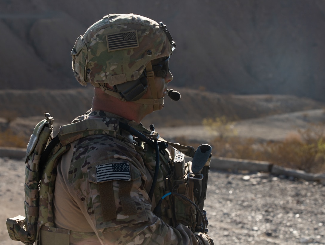 A soldier wearing a helmet, holding a gun and dressed in camouflage gazes into the distance while conducting a patrol over rocky terrain.