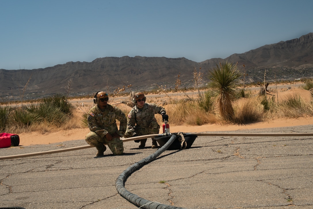 Two soldiers watch over three hoses during a refueling operation.
