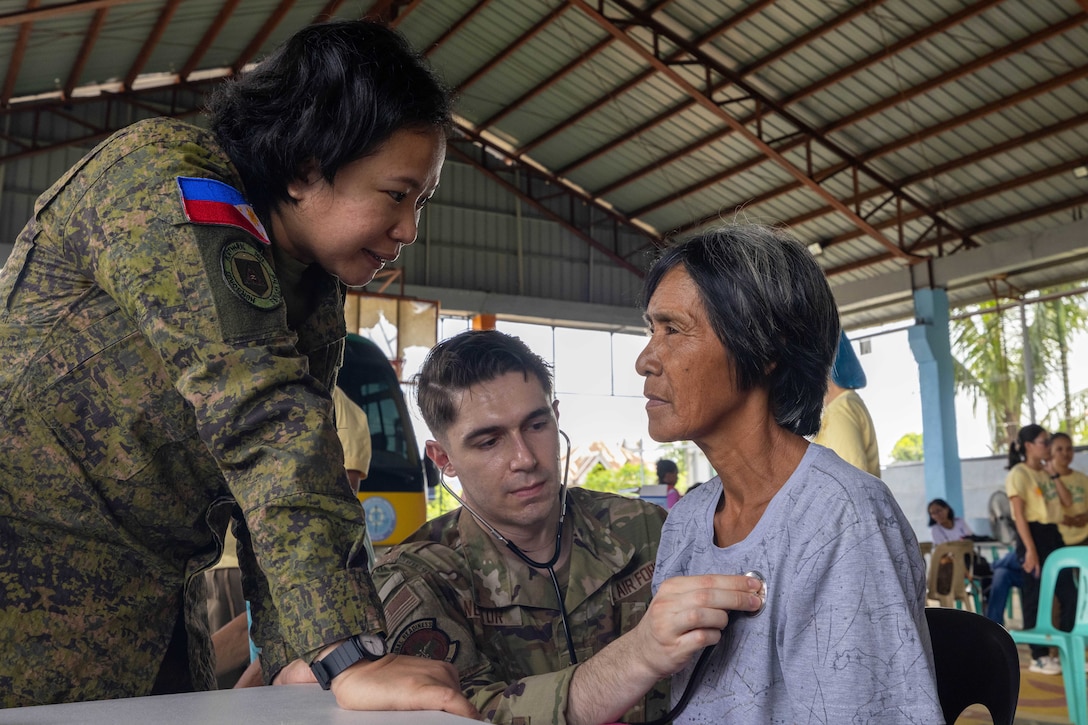 Two military service members, one U.S. and the other Philippine, assess a civilian indoors.