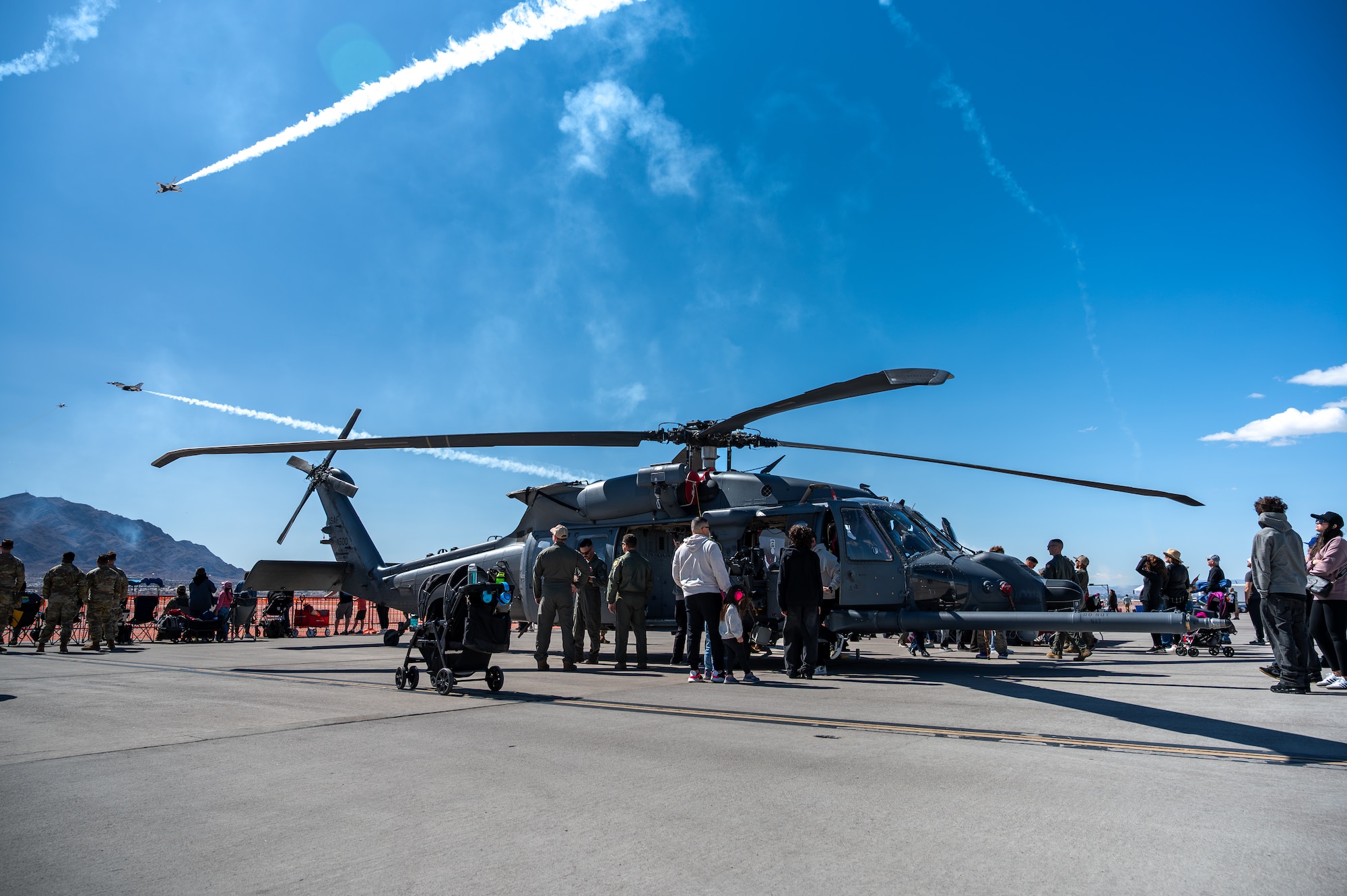Guests at Aviation Nation 2025 explore inside an HH-60W Jolly Green II helicopter while the U.S. Air Force Thunderbirds perform an aerial display during Aviation Nation 2025 at Nellis Air Force Base, Nevada, April 4, 2025.