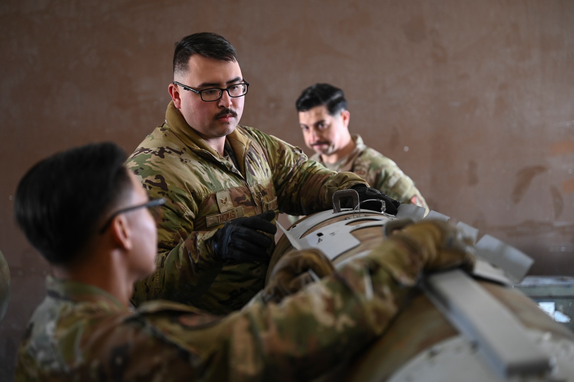 Senior Airman Scott Thomas, 8th Maintenance Squadron Munitions Flight conventional maintenance crew chief, and Airmen from the 8th practice installing panels on a training munition.