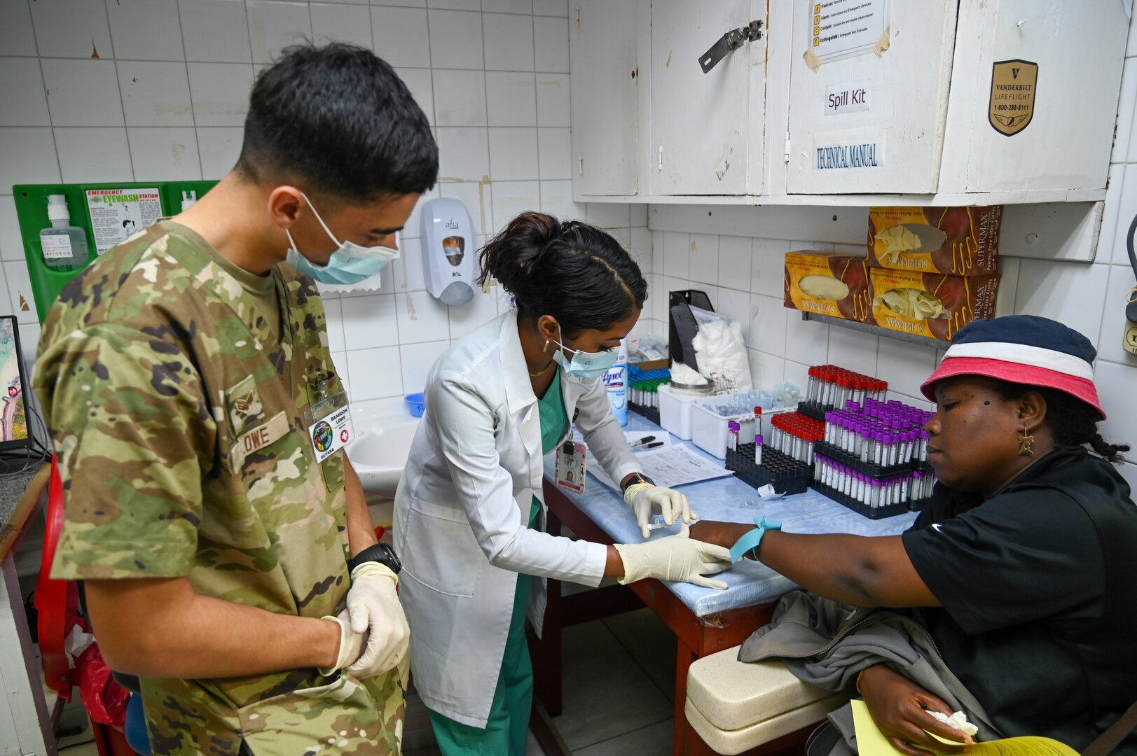 U.S. Air Force Senior Airman Brandon Lowe, 433rd Aeromedical Staging Squadron medical technician, observes while Julia Ann Sarjoo, Georgetown Public Hospital phlebotomist, takes blood from a patient at the Georgetown Public Hospital during the Lesser Antilles Medical Assistance Team mission in Georgetown, Guyana, April 2, 2025.