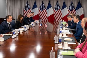 People sit around a table on either side while at the end of the room U.S. and French flags rest.