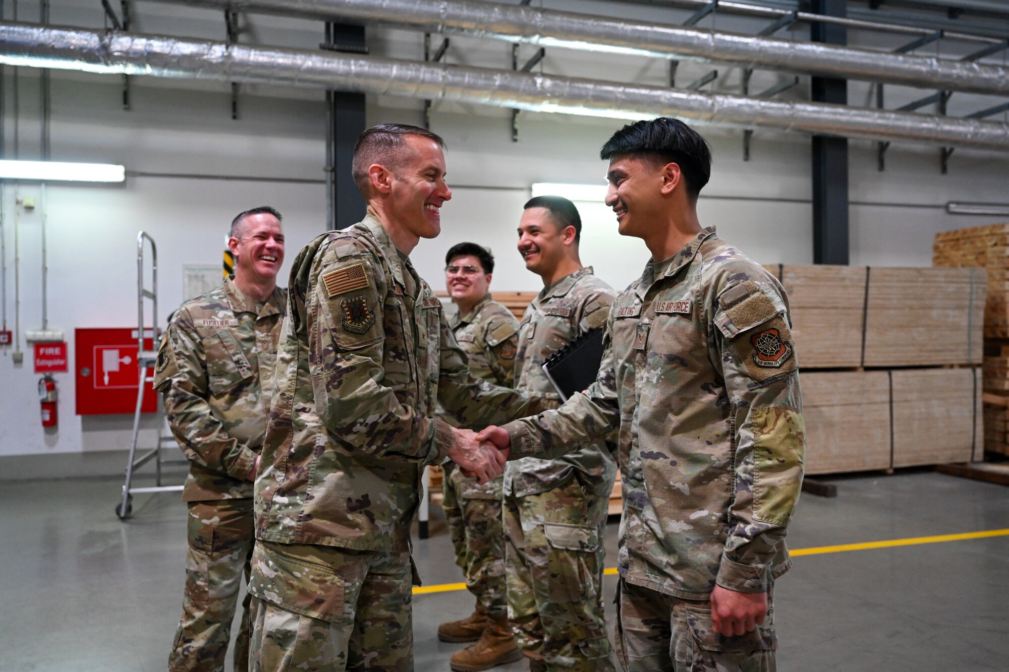 Brig. Gen. Stephen Snelson, left, U.S. Air Force Expeditionary Center commander, coins Senior Airman Patrick Palting, a 721 Aerial Port Squadron special handling specialist, at the 721 APS throughput building during an immersion tour on Ramstein Air Base, Germany, April 11, 2025.