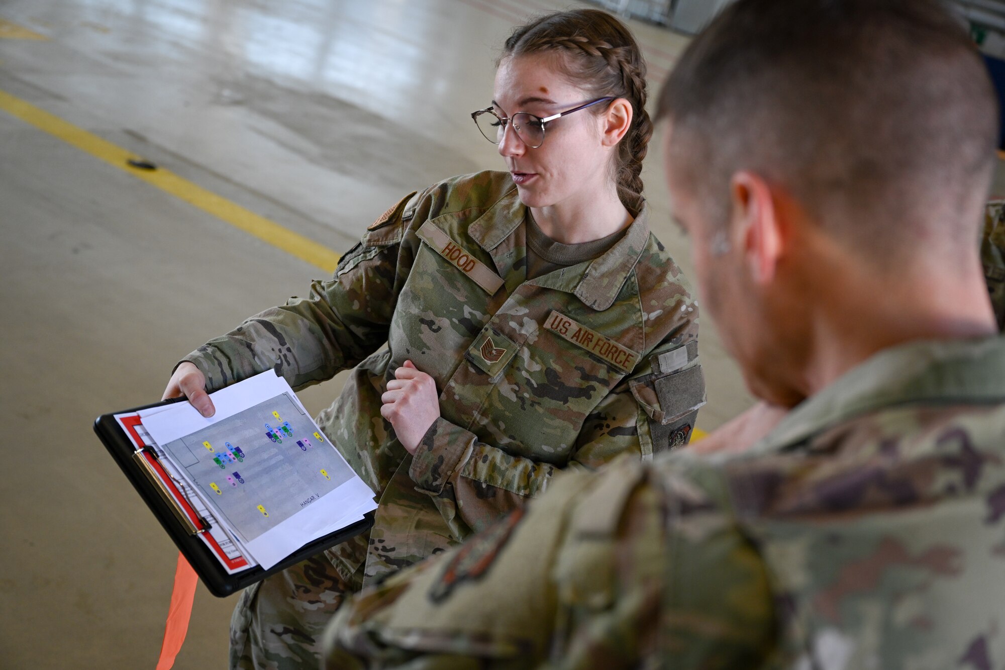 Tech. Sgt. Alannah Hood, center, 721st Aircraft Maintenance Squadron facility manager, shows Brig. Gen. Stephen Snelson, right, U.S. Air Force Expeditionary Center commander, a chart of facility items outlined for awareness in Hangar 5 on Ramstein Air Base, Germany, April 11, 2025.