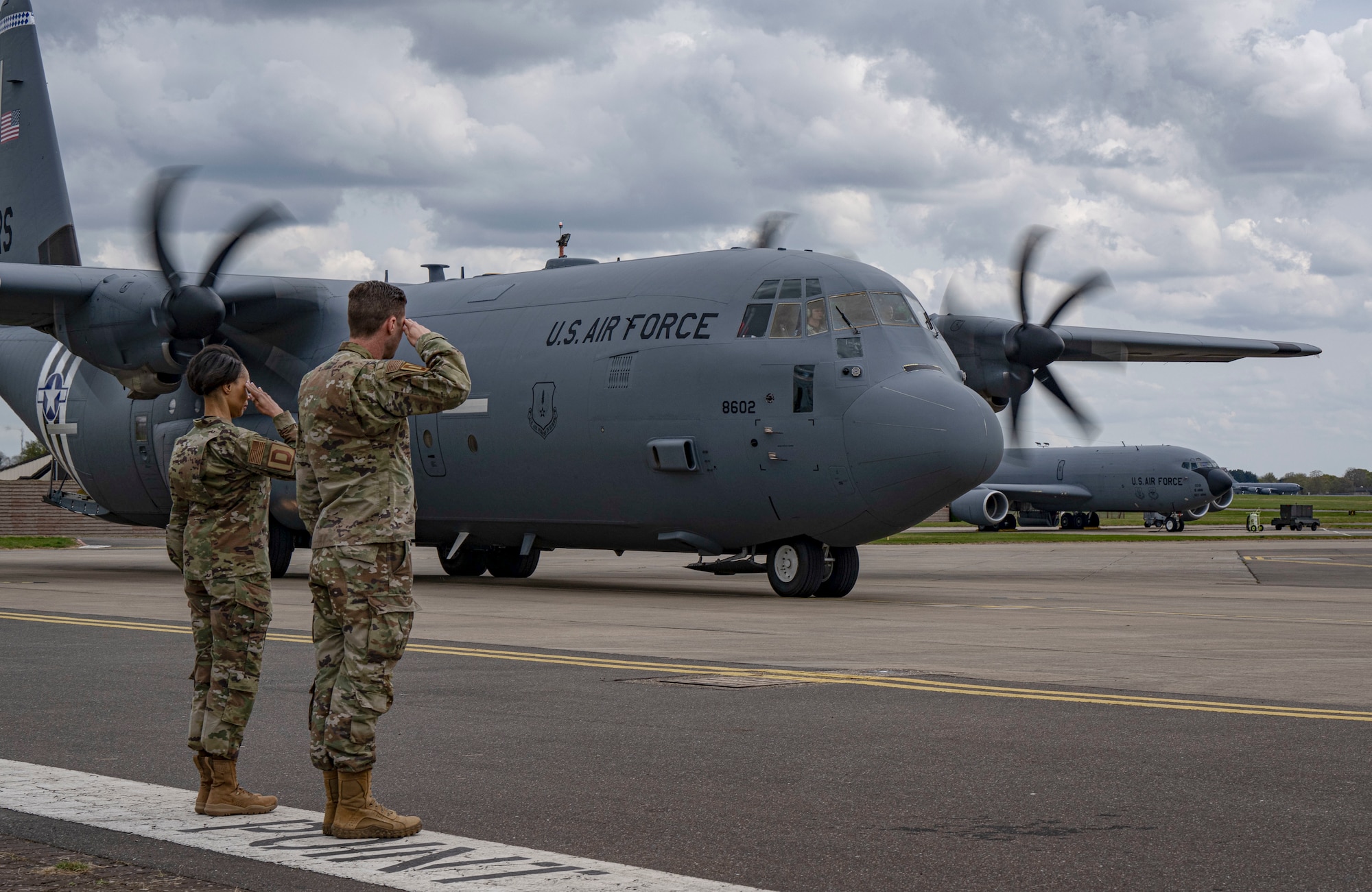 U.S. Air Force Chief Master Sgt. Tiffany Griego, left, 100th Air Refueling Wing command chief, and Col. Ryan Garlow, 100th ARW commander, render salutes as a C-130J Super Hercules containing Gen. James Hecker, U.S. Air Forces in Europe - Air Forces Africa commander, arrives at RAF Mildenhall, England, April 14, 2025.
