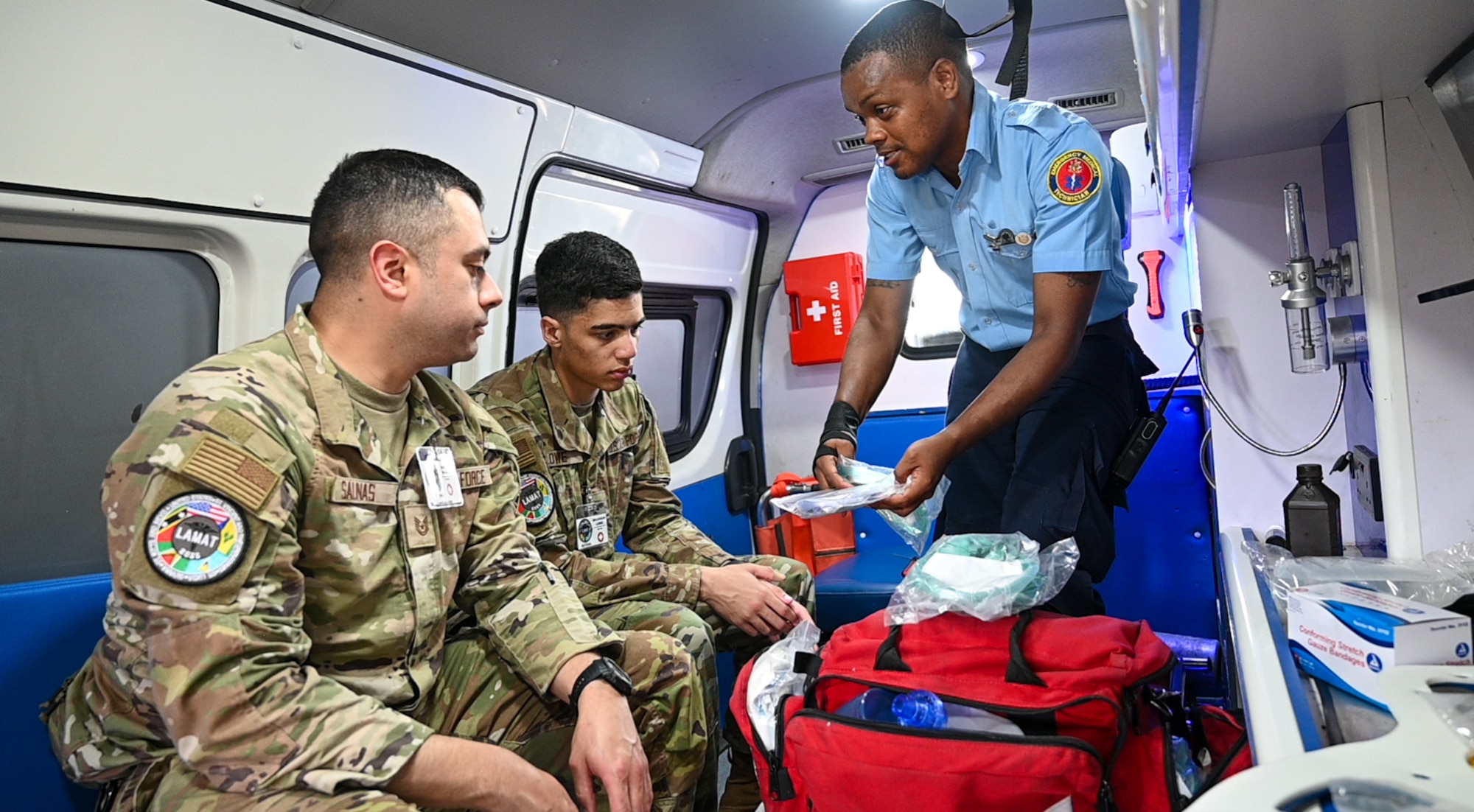 U.S. Air Force Tech. Sgt. Rodrigo Salinas, 433rd Aeromedical Staging Squadron medical technician, and U.S. Air Force Senior Airman Brandon Lowe, 433rd Aeromedical Staging Squadron medical technician, learn from Cleveland King, a Guyana Fire and Emergency Medical Service advanced emergency medical technician training officer, about the equipment and protocol procedures for EMTs on an ambulance at the Guyana Fire Service Headquarters during the Lesser Antilles Medical Assistance Team mission in Georgetown, Guyana, April 3, 2025.