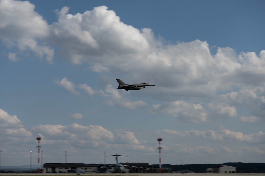 An F-16 flying over a flightline.