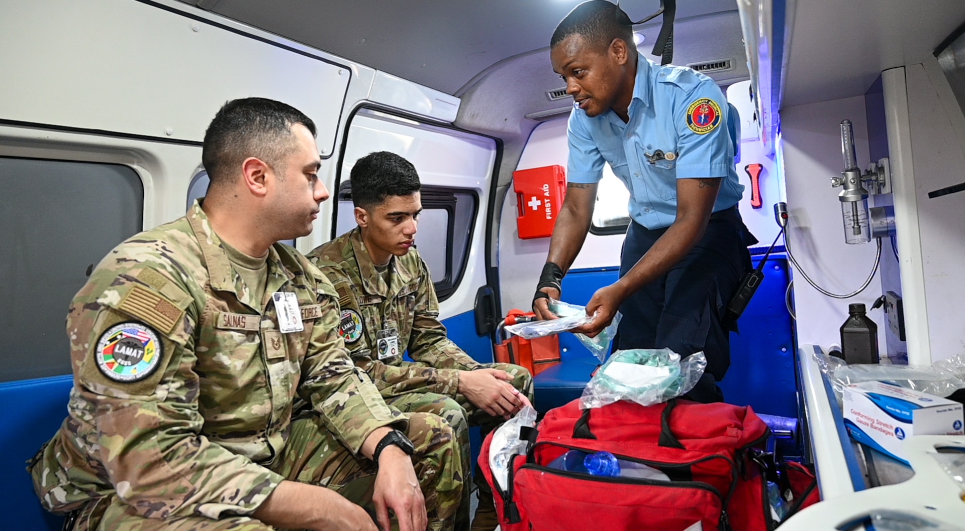 U.S. Air Force Tech. Sgt. Rodrigo Salinas, 433rd Aeromedical Staging Squadron medical technician, and U.S. Air Force Senior Airman Brandon Lowe, 433rd Aeromedical Staging Squadron medical technician, learn from Cleveland King, a Guyana Fire and Emergency Medical Service advanced emergency medical technician training officer, about the equipment and protocol procedures for EMTs on an ambulance at the Guyana Fire Service Headquarters during the Lesser Antilles Medical Assistance Team mission in Georgetown, Guyana, April 3, 2025.
