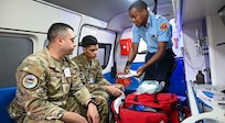 U.S. Air Force Tech. Sgt. Rodrigo Salinas, 433rd Aeromedical Staging Squadron medical technician, and U.S. Air Force Senior Airman Brandon Lowe, 433rd Aeromedical Staging Squadron medical technician, learn from Cleveland King, a Guyana Fire and Emergency Medical Service advanced emergency medical technician training officer, about the equipment and protocol procedures for EMTs on an ambulance at the Guyana Fire Service Headquarters during the Lesser Antilles Medical Assistance Team mission in Georgetown, Guyana, April 3, 2025.
