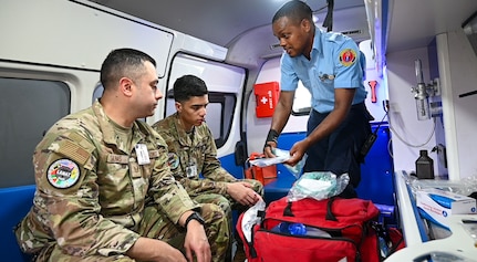 U.S. Air Force Tech. Sgt. Rodrigo Salinas, 433rd Aeromedical Staging Squadron medical technician, and U.S. Air Force Senior Airman Brandon Lowe, 433rd Aeromedical Staging Squadron medical technician, learn from Cleveland King, a Guyana Fire and Emergency Medical Service advanced emergency medical technician training officer, about the equipment and protocol procedures for EMTs on an ambulance at the Guyana Fire Service Headquarters during the Lesser Antilles Medical Assistance Team mission in Georgetown, Guyana, April 3, 2025.