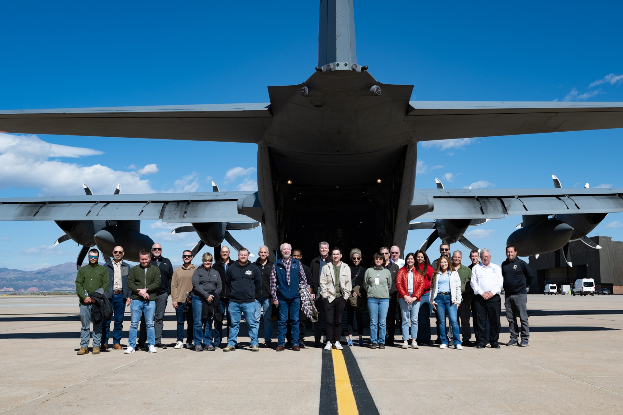 A row of civilians standing outside the rear of a military aircraft.
