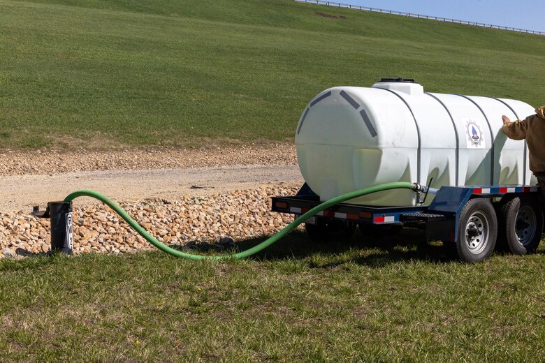 A green hose sticks out of a metal tube with a large white water tank to the right.