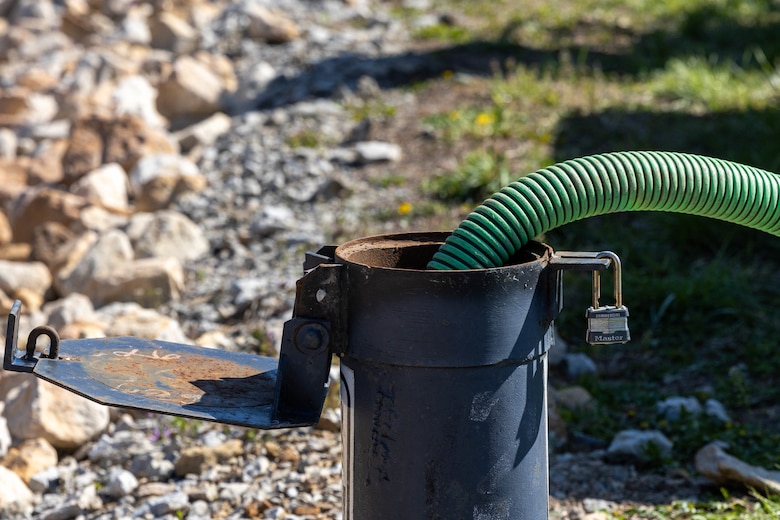 A green hose sticks out of a metal tube with rocks in the background.