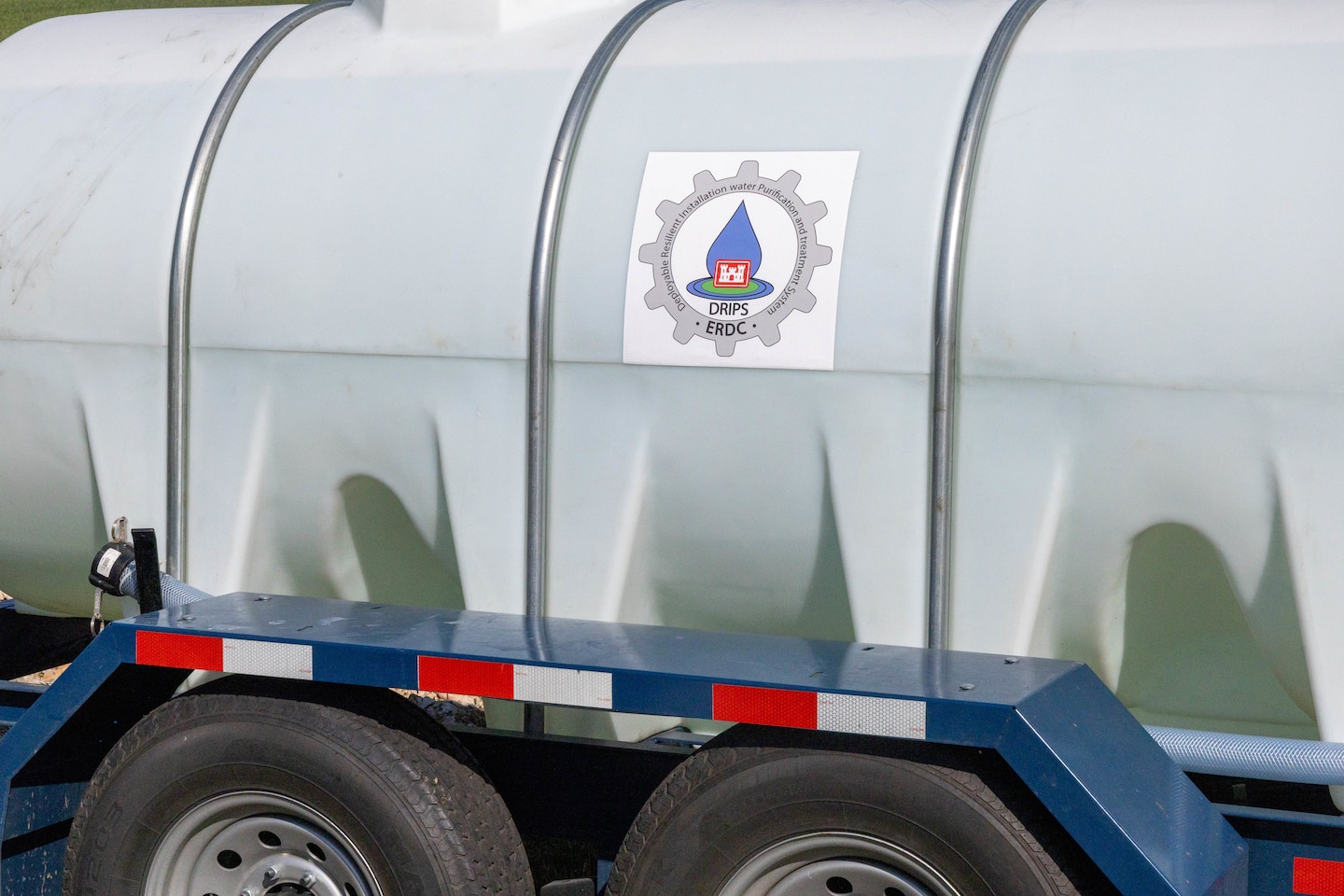 A white plastic water tank sits on a blue trailer.
