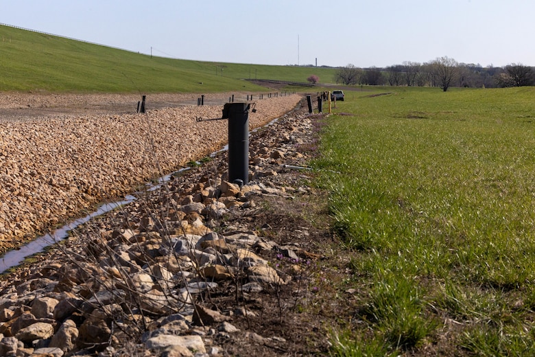 Metal tubes stick out of the ground with rock on the left and grass on the right.