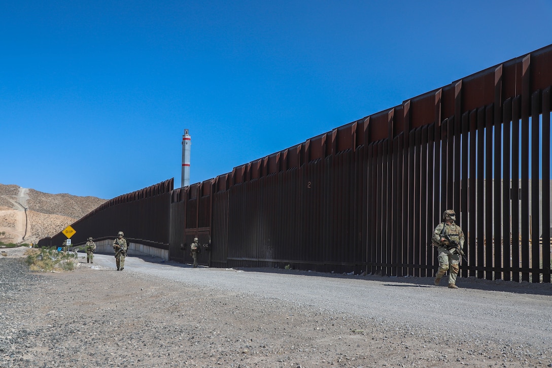 Soldiers patrol along a large wall in the desert.
