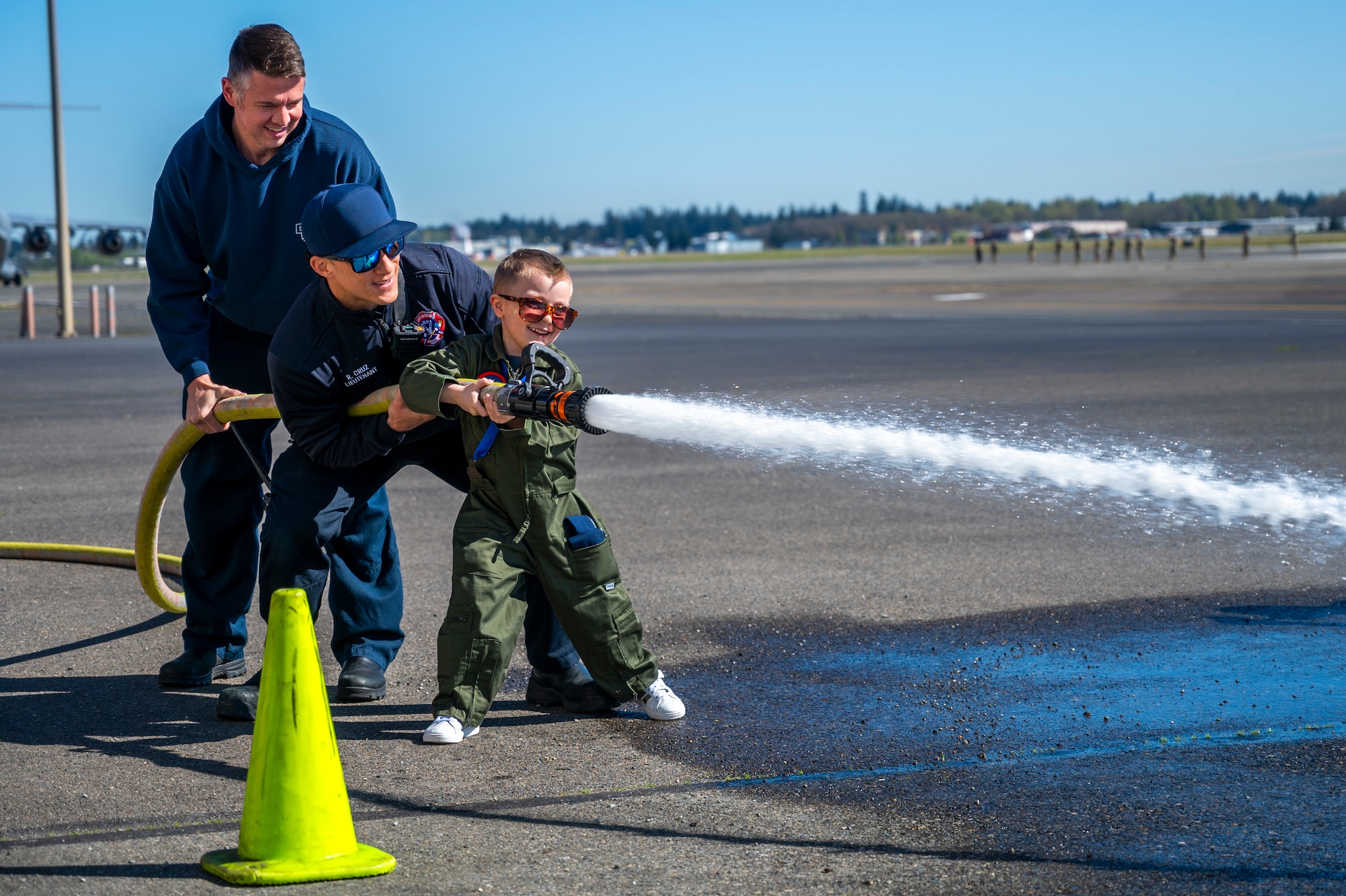 Benny Blankenship, the 2025 Team McChord pilot for a day, right, Ray Cruz, Joint Base Lewis-McChord Fire and Emergency Services lieutenant, center, and Jeremiah Hanna-Cruz, JBLM Fire and Emergency Services fire fighter, spray water from a fire hose at JBLM, Washington, April 17, 2025.