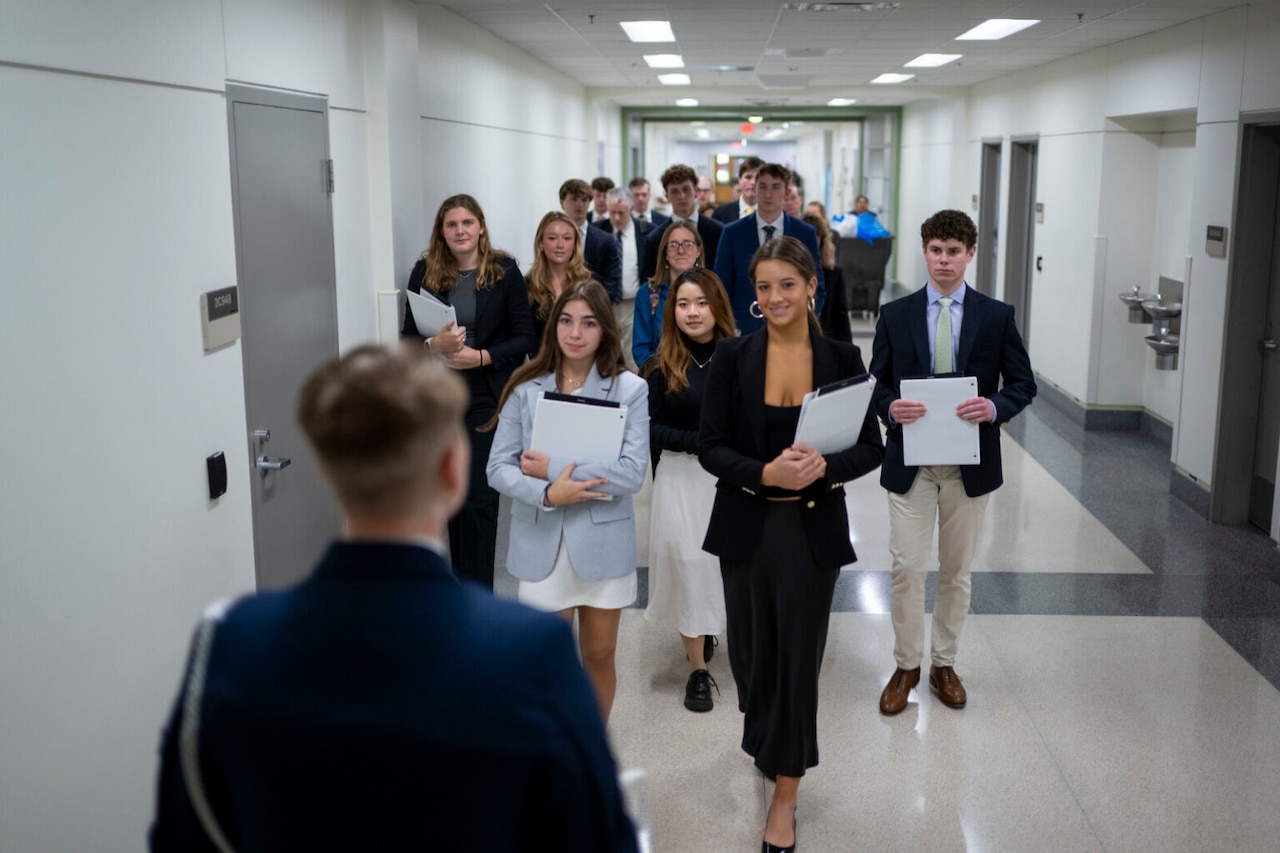 A group of young people in business attire walk down a hallway.