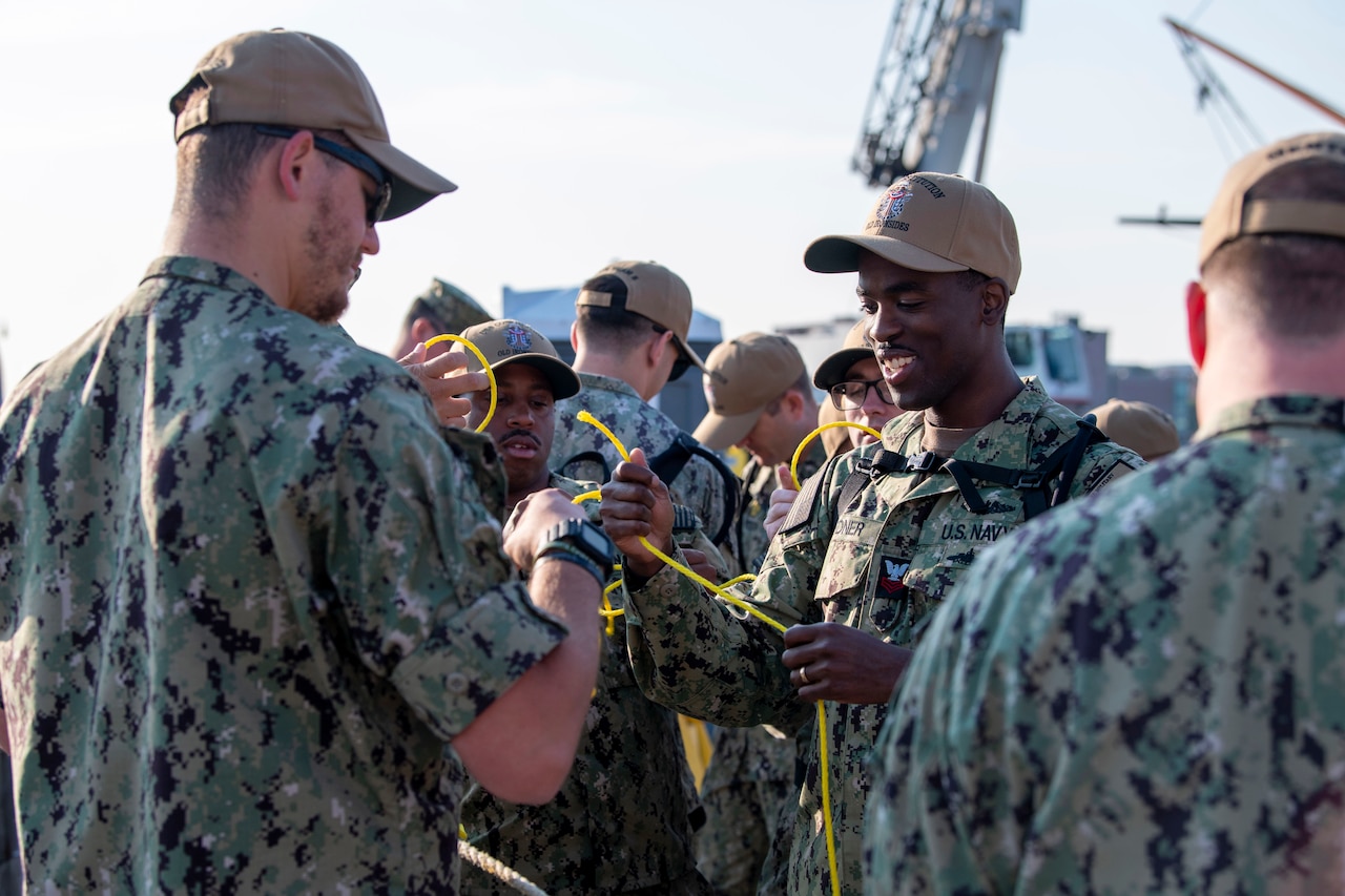 A group of sailors practice tying knots.