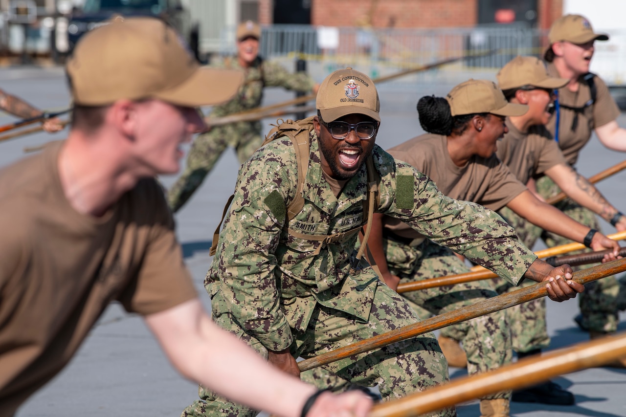 A group of sailors practice with spears outside.