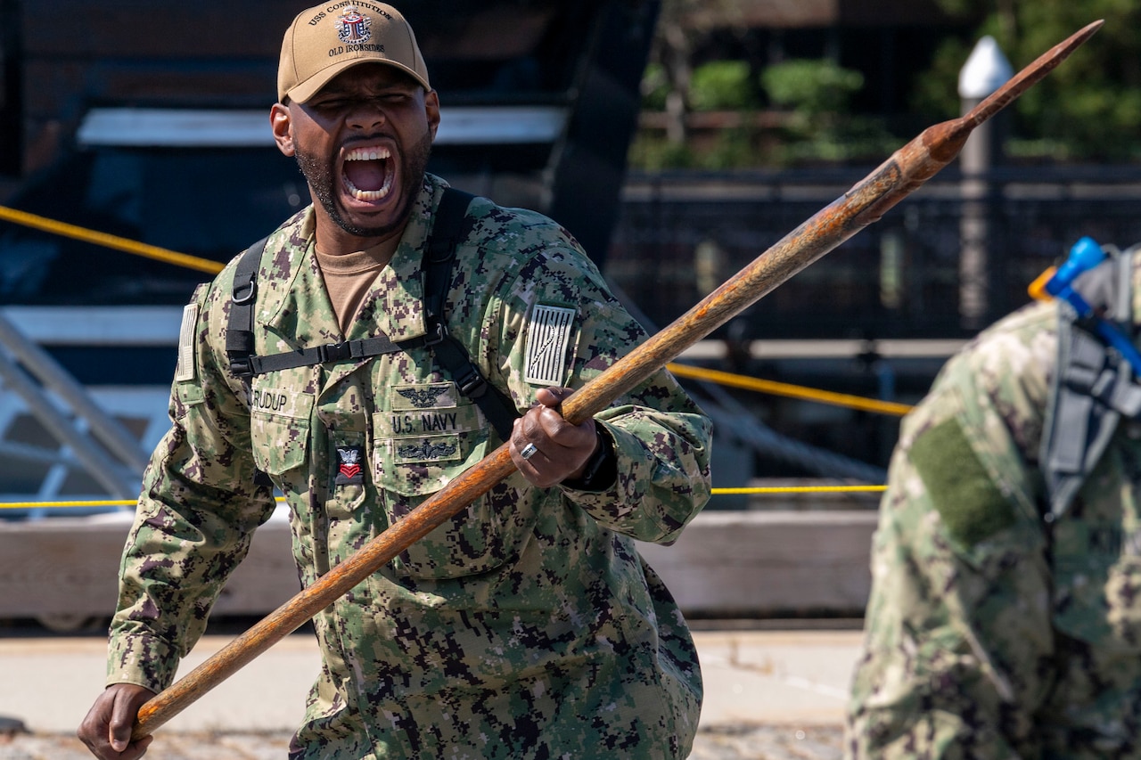 A sailor holding a spear simulates a battle cry.