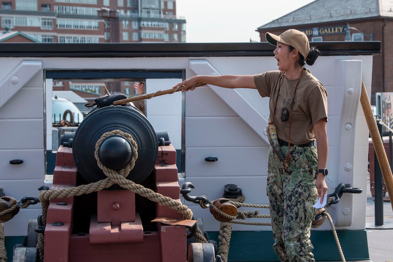 A sailor pretends to light a canon outside.