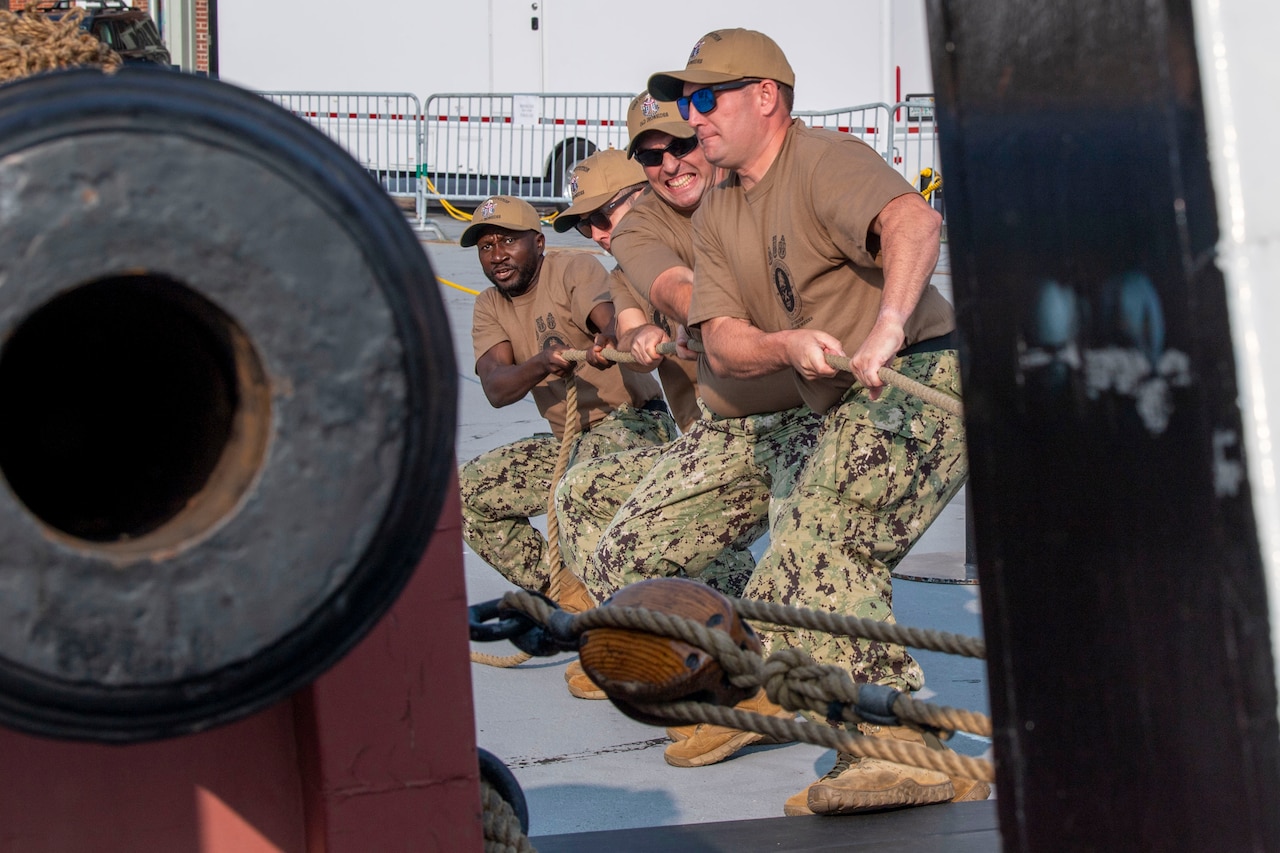 Four sailors pull ropes attached to an old canon.