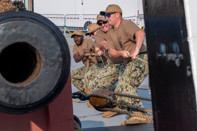 Four sailors pull ropes attached to an old canon.