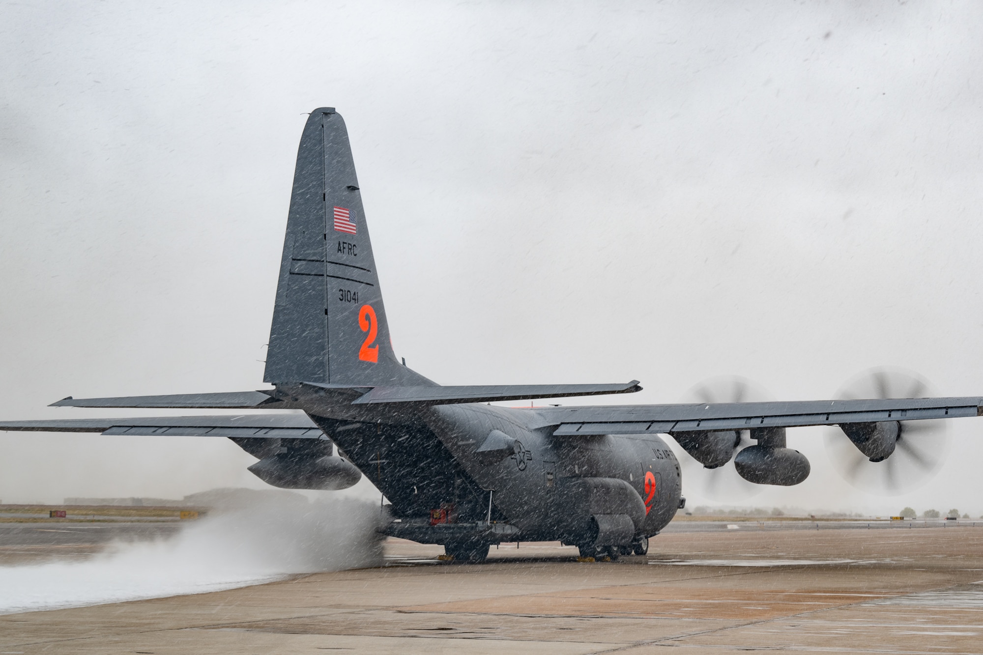 A military aircraft with its engines running emits a burst of water onto the concrete.