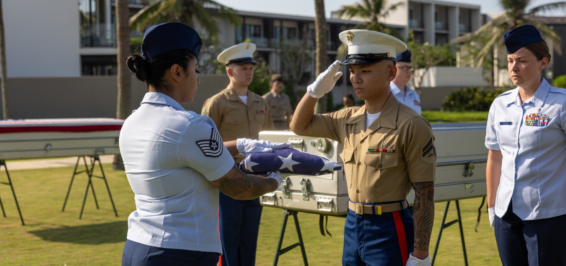 U.S. Air Force Tech. Sgt. Fanny Solano, team medic and short-term individual augmentee, Defense POW/MIA Accounting Agency, presents a U.S. flag while U.S. Marine Corps Cpl. Kevin Nguyen, recovery noncommissioned officer and short-term individual augmentee, DPAA, renders a salute during a repatriation ceremony in Vietnam, April 19, 2025.