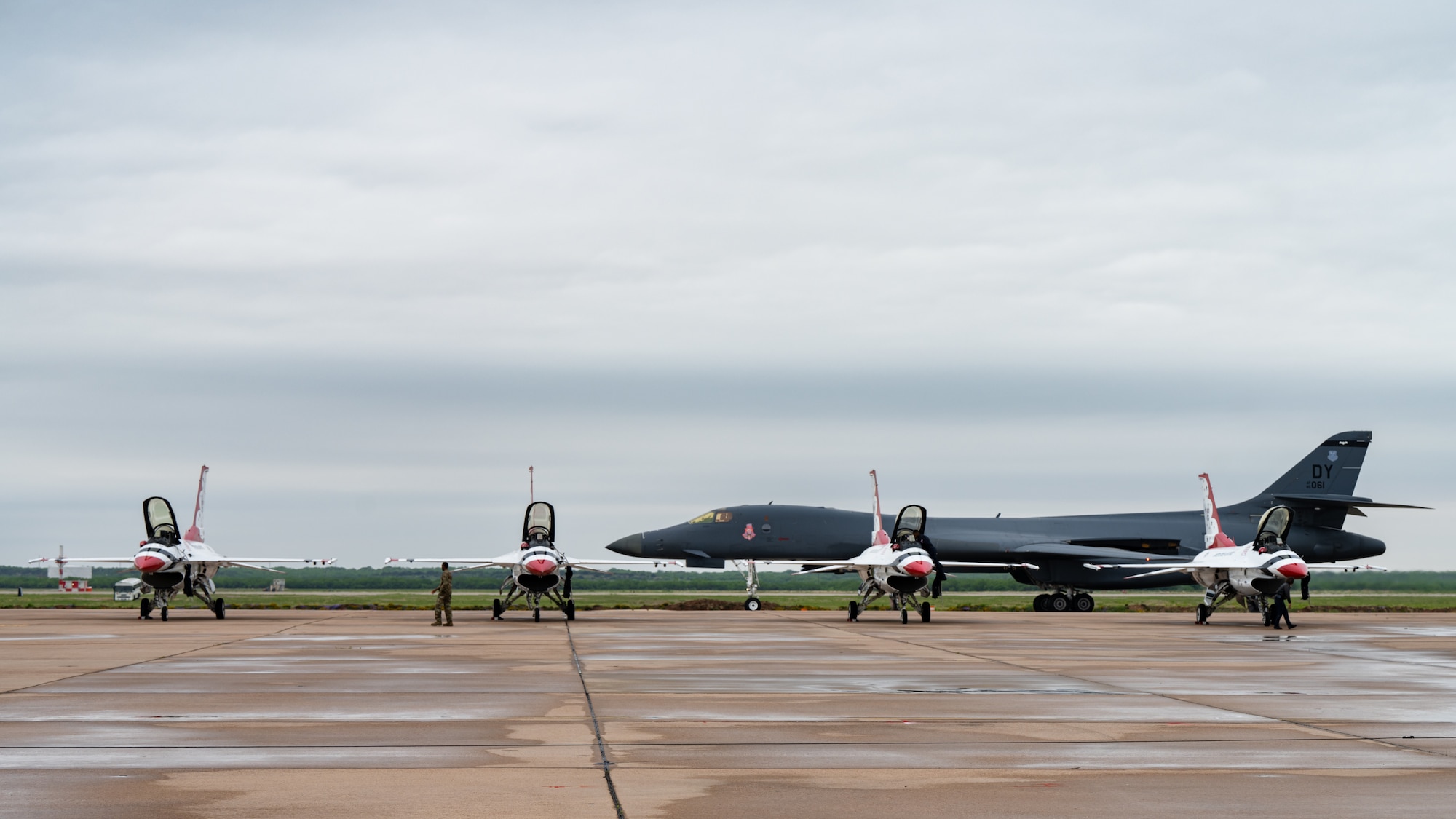 a b-1 taxis on the flightline behind four f-16s parked on the flightline