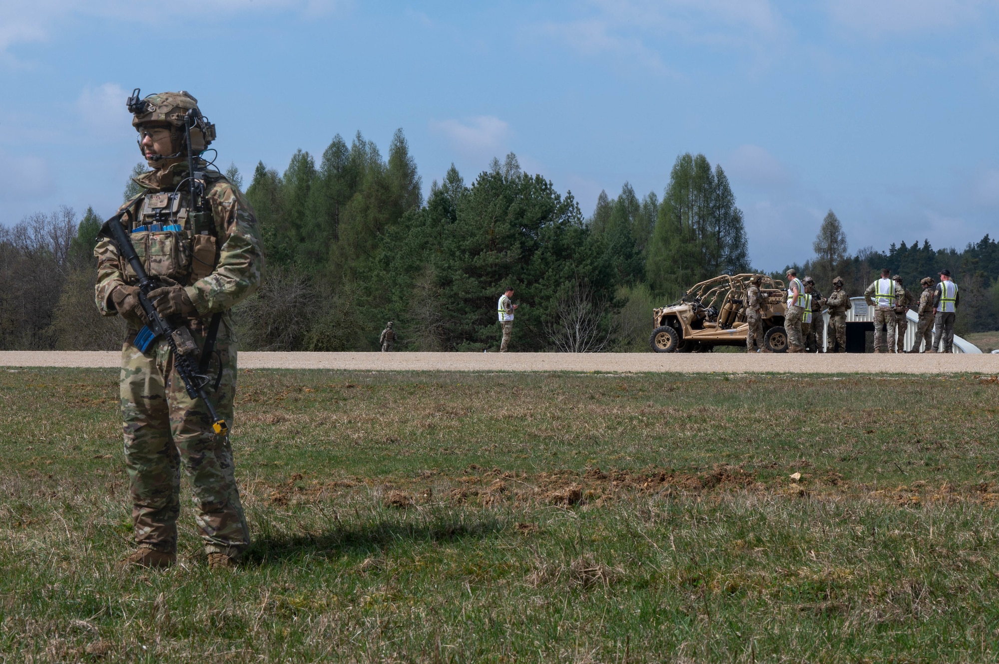 A man pulls security while people prepare for a sling load operation