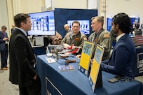 Lt. Cmdr. Patrick Heitman (center-right) and Lt. Sean Carpenter (center-left) from the U.S. Naval Research Laboratory Scientific Development Squadron One (VXS-1) discuss squadron capabilities at the 2025 Sea Air Space expo in National Harbor, Md. April 8, 2025. VXS-1 conducts airborne scientific experimentation and advanced technology development in worldwide operations supporting U.S. Navy and national science and technology priorities and war fighting goals. (U.S. Navy photo by Sarah Peterson)