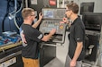 Two men are seen working on a machine.
