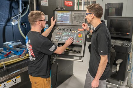 Two men are seen working on a machine.