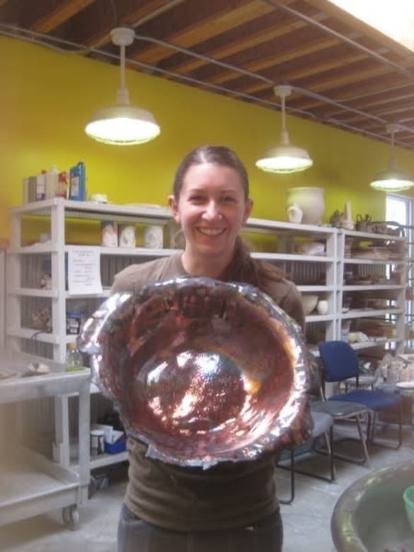 A female college student holds a ceramic bowl inside an art studio.