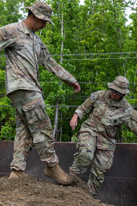 Two soldiers stamp around on gravel on top of a dump truck.