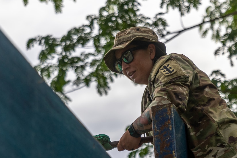 A soldier leans over the side of a dump truck during an overcast day.