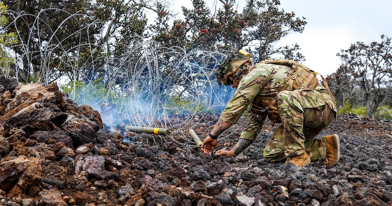 A Soldier is next to barbwire on setting up explosive charges to remove the obstructing wire.