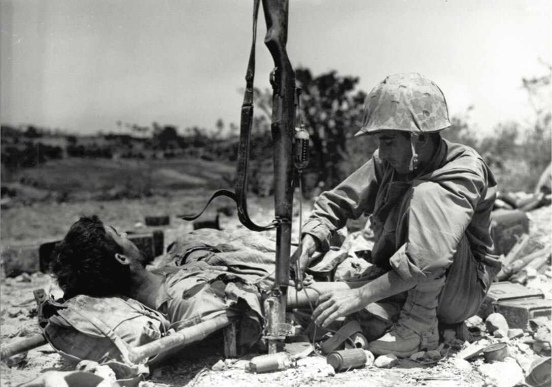 Wounded Marine gets injection of blood plasma from Navy Hospital Corpsman during battle for Okinawa, Japan. The corpsman is using the rifle as a plasma holder.