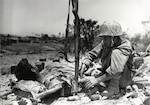 Wounded Marine gets injection of blood plasma from Navy Hospital Corpsman during battle for Okinawa, Japan. The corpsman is using the rifle as a plasma holder.