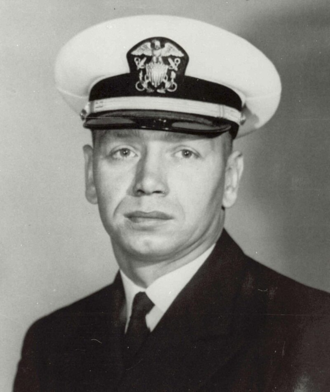 A man in a military dress uniform and dress cap poses for a photo.