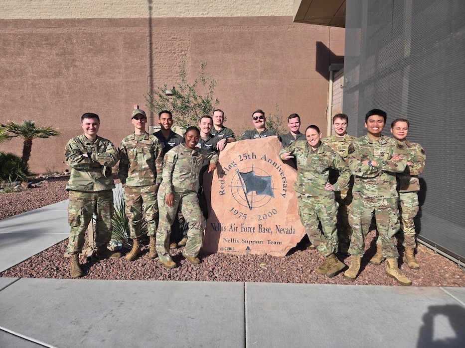 Airmen stand in a group for a photo around a statue emblazoned with the Red Flag logo.