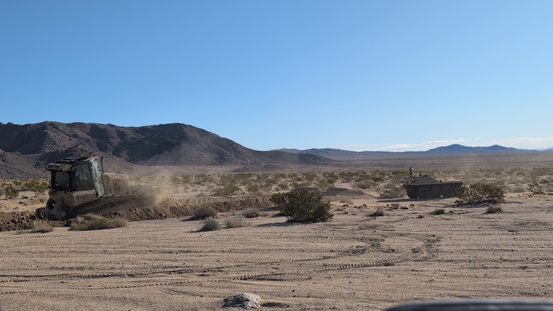While the Robotics for Engineer Operations (REO) Engineer Site Characterization Demonstrator (SCD) provides overwatch, ERDC REO's unmanned bulldozer, created by a collaborative team of engineers from CERL, GSL, GRL and ITL, builds a fighting position in support of operational forces.
