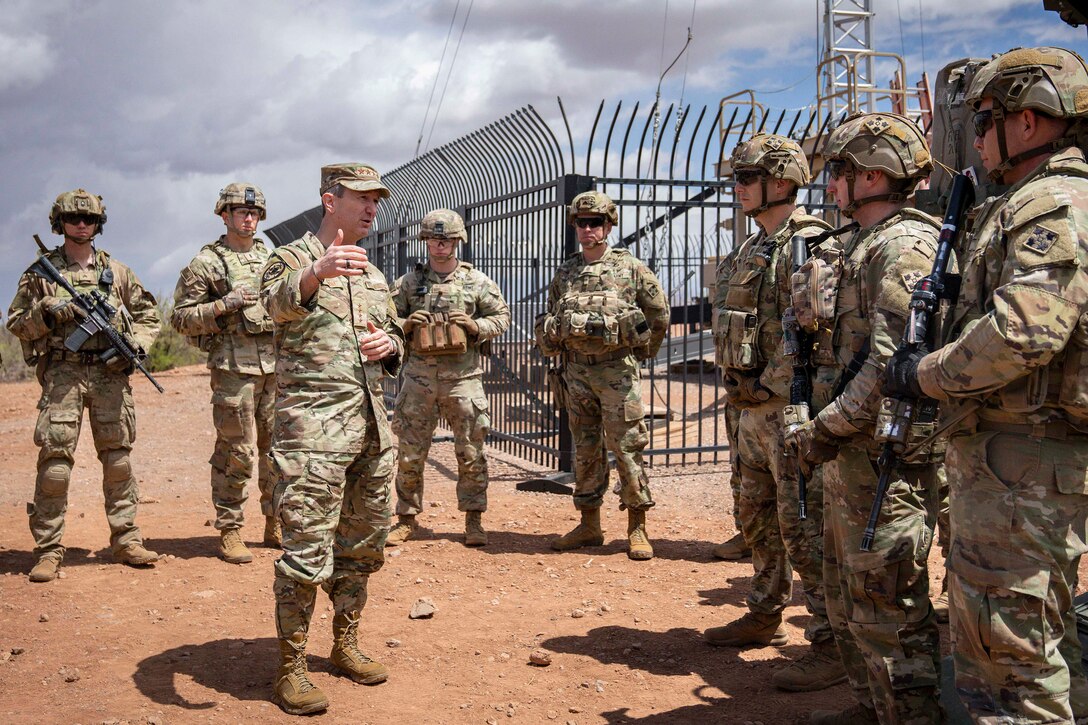 Chairman of the Joint Chiefs of Staff Air Force Gen. Dan Caine talks to troops outdoors.